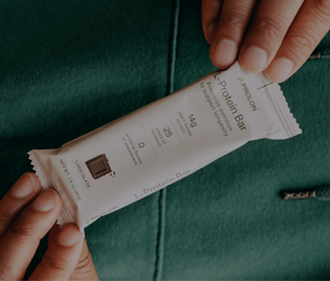 Protein bar packaging held by a person against a green background