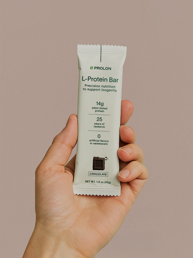 Hand holding a L-Protein Bar package against a beige background